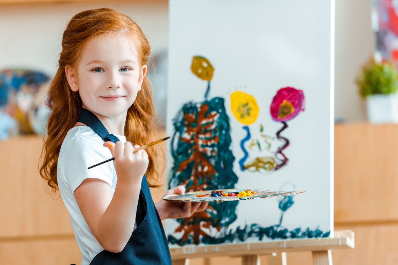 Lachendes rothaariges Mädchen, das neben einem Gemälde auf Leinwand steht