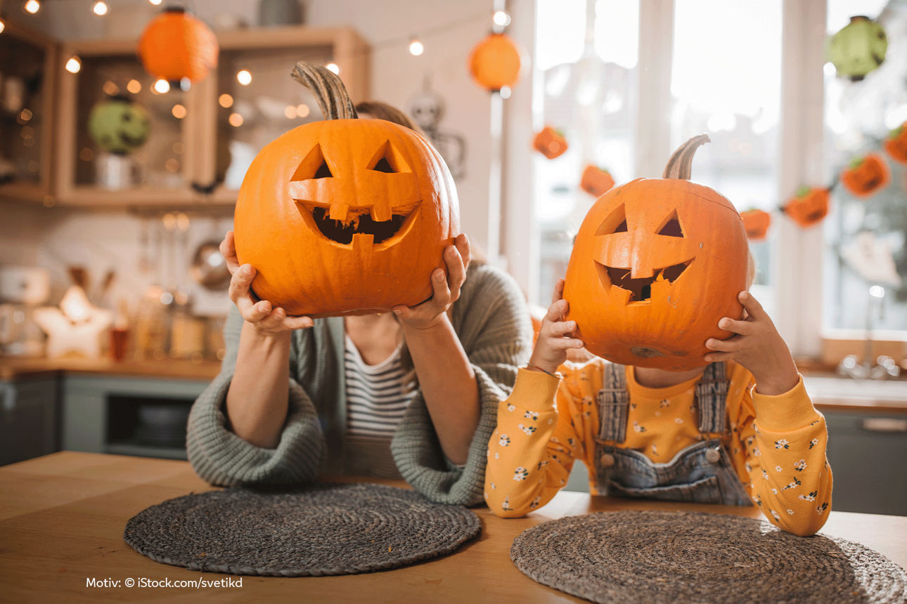 Eine erwachsene Person und ein Kind halten jeweils einen geschnitzten Halloween-Kürbis vor ihr Gesicht