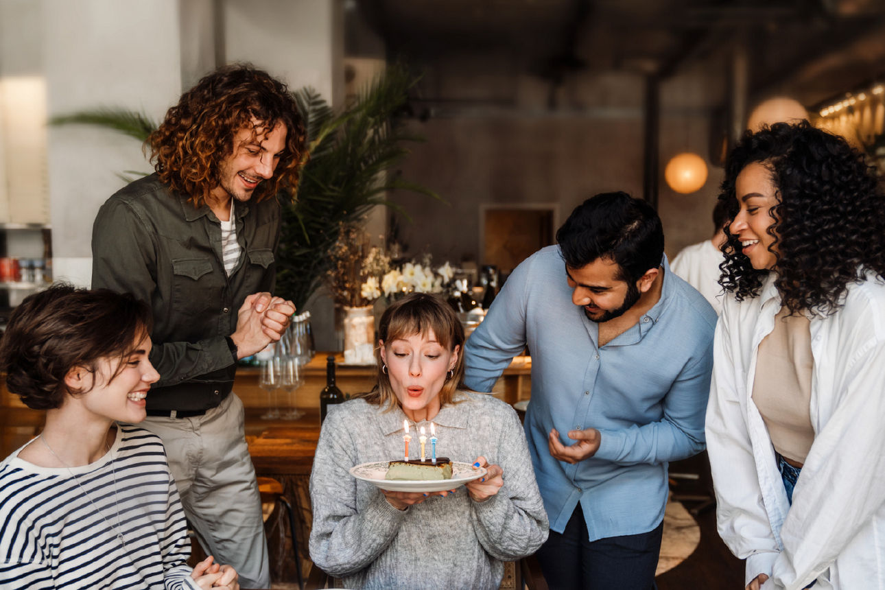 Familie sitzt am Tisch, feiert Geburtstag, Frau pustet Kerze aus.