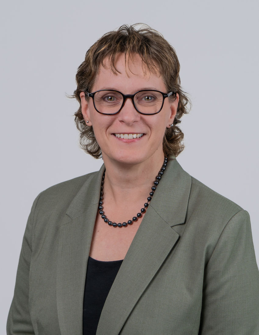 Foto unserer Vermögensberaterin Kerstin Braun vor einem grauen Hintergrund in einem grünen Blazer