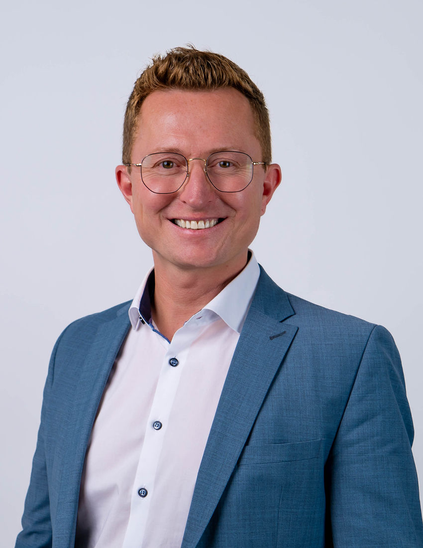Foto unseres Vermögensberaters Fabian Ellmann vor einem grauen Hintergrund in einem blauen Sakko