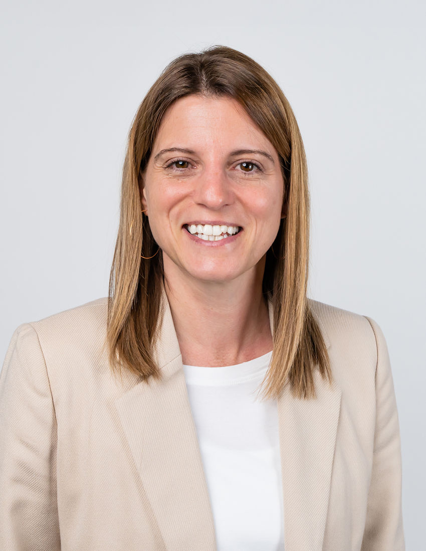 Foto unserer Vermögensberaterin Nicole Münzberg vor einer weißen Wand in einem beigen Blazer
