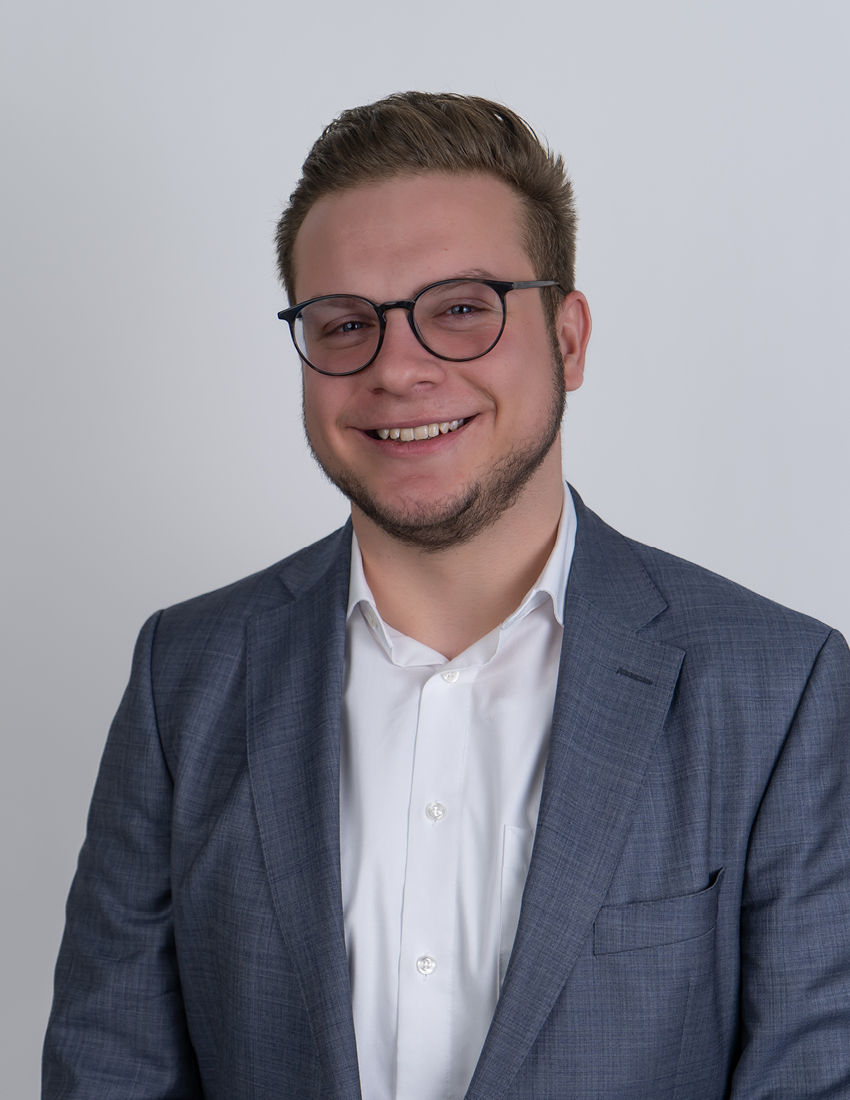 Foto unseres Vermögensberaters Moritz Richter vor einem grauen Hintergrund in einem grauen Sakko