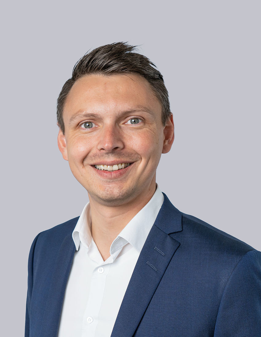 Foto unseres Vermögensberaters Stefan Serek vor einem grauen Hintergrund in einem dunkelblauen Sakko