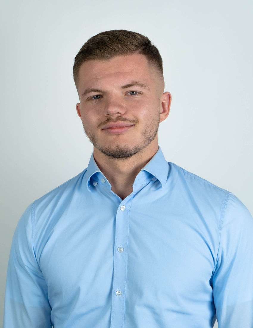 Foto unseres Vermögensberaters Hendrik Stäblein vor einem grauen Hintergrund in einem blauen Hemd