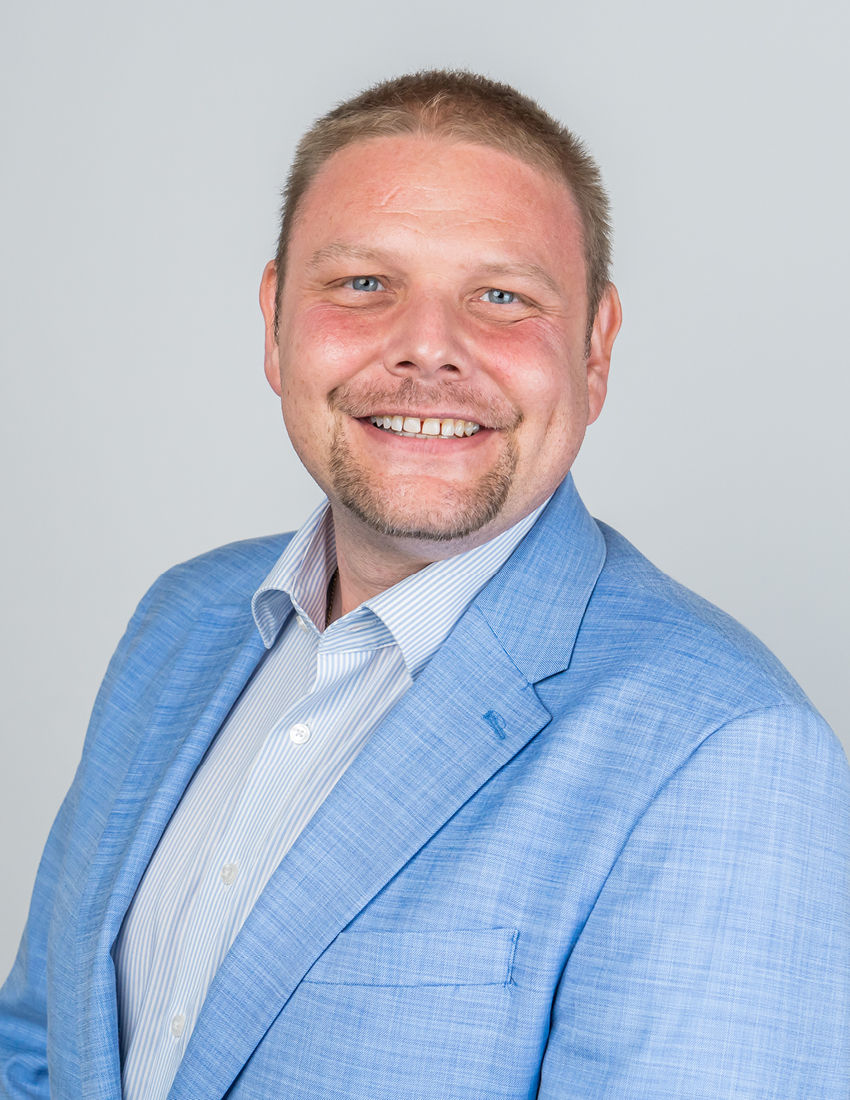 Foto unseres Vermögensberaters Andre Zurek vor einem grauen Hintergrund in einem hellblauen Jackett