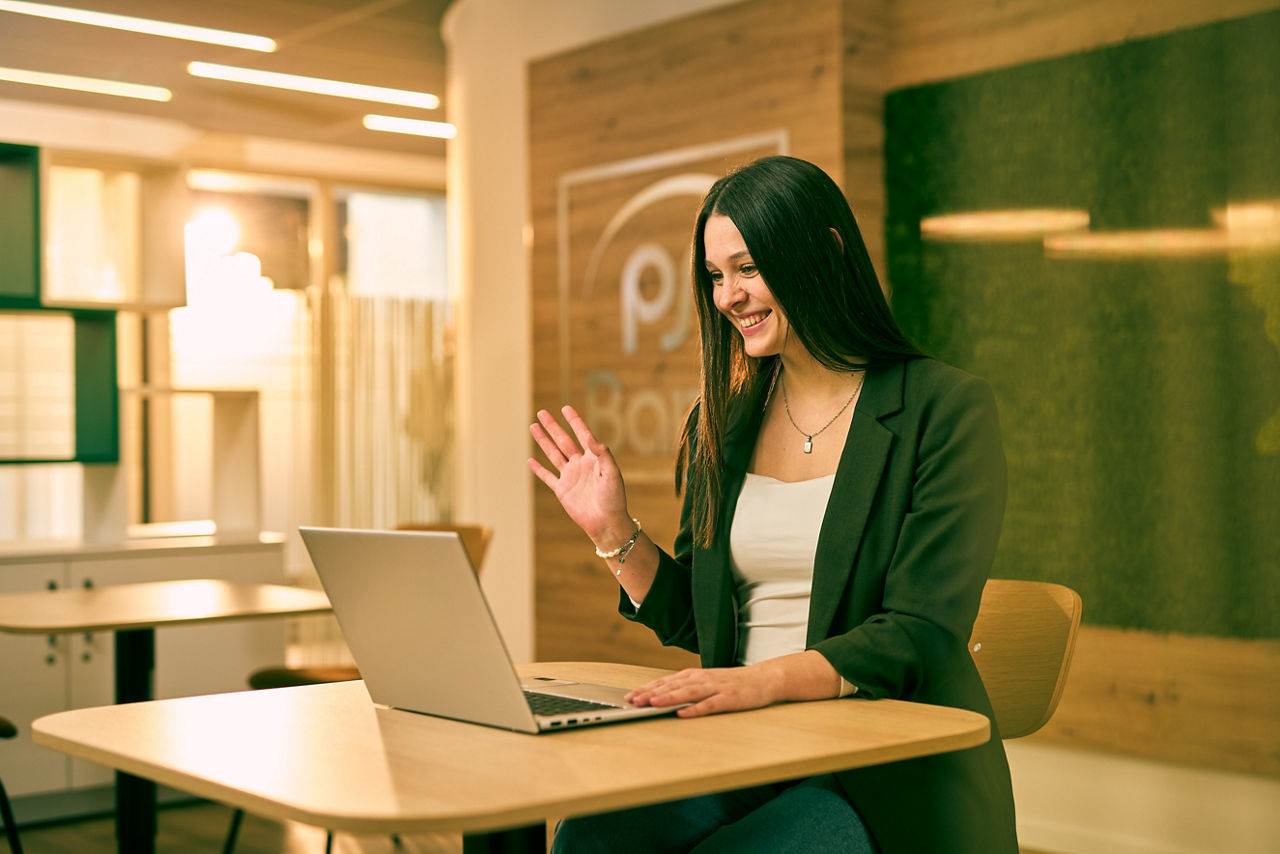 Mitarbeiterin der Bank winkt in ihren Latop den anderen Meeting Teilnehmern zu.
