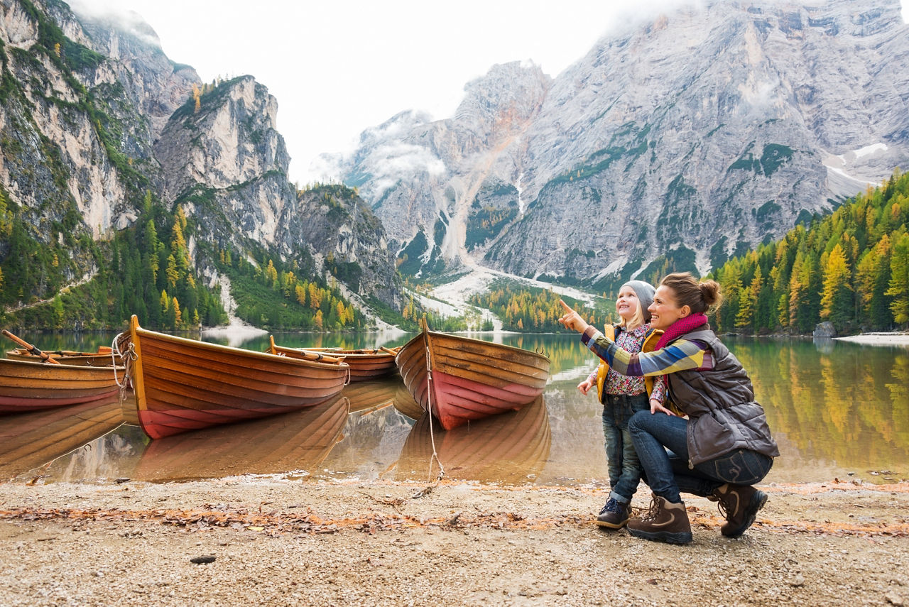 Mutter zeigt dem Kind die schöne Landschaft am See. Im Hintergrund sind Berge.