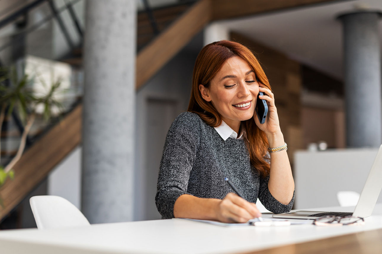 Eine Frau mit grauem Pullover sitzt mit einem Laptop am Schreibtisch.