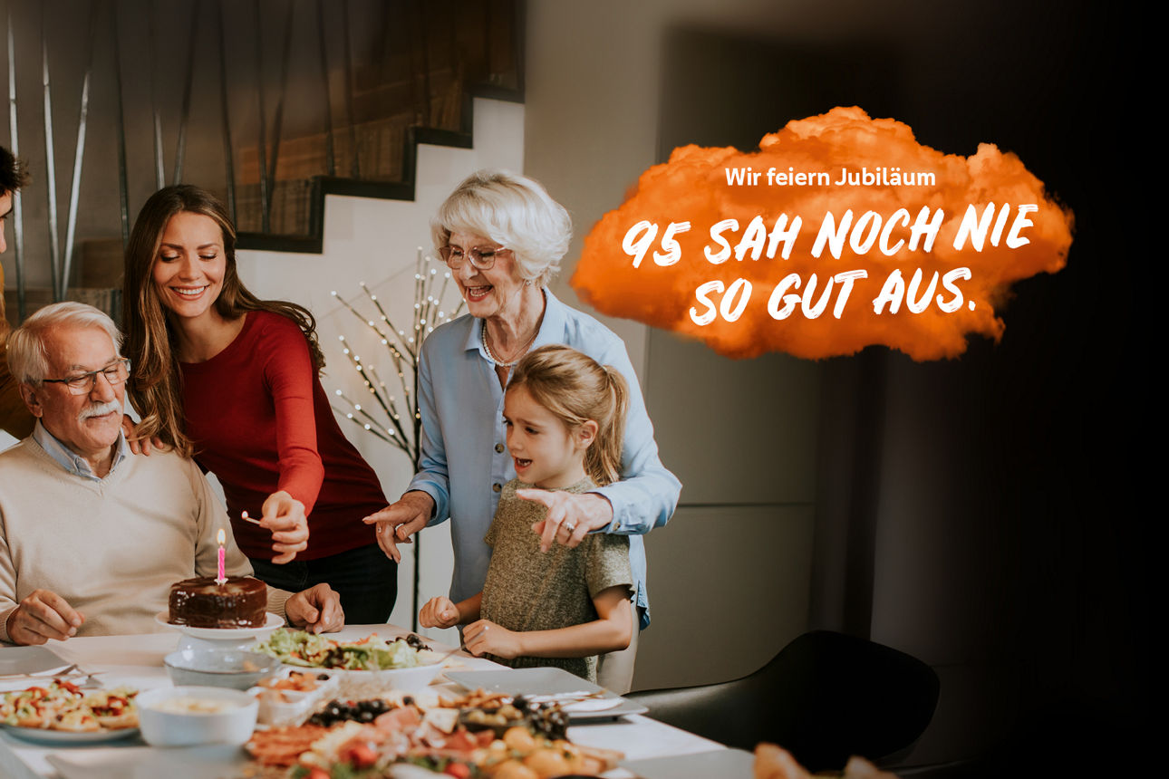 .Eine Familie feiert Geburtstag mit einer Torte an einem Tisch. Die Frau zündet die Kerze an.