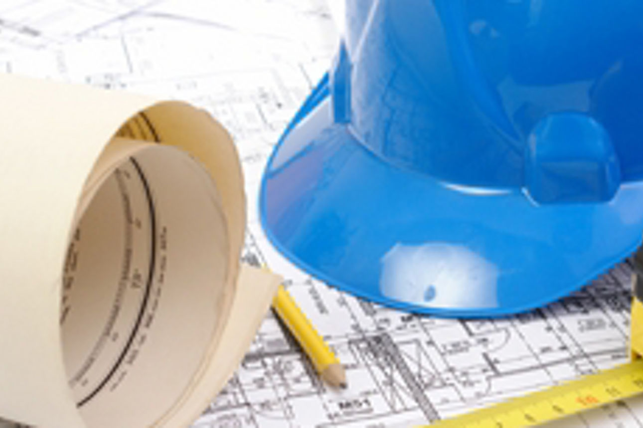 Baupläne, ein blauer Schutzhelm und ein Lineal liegen auf einer Fläche