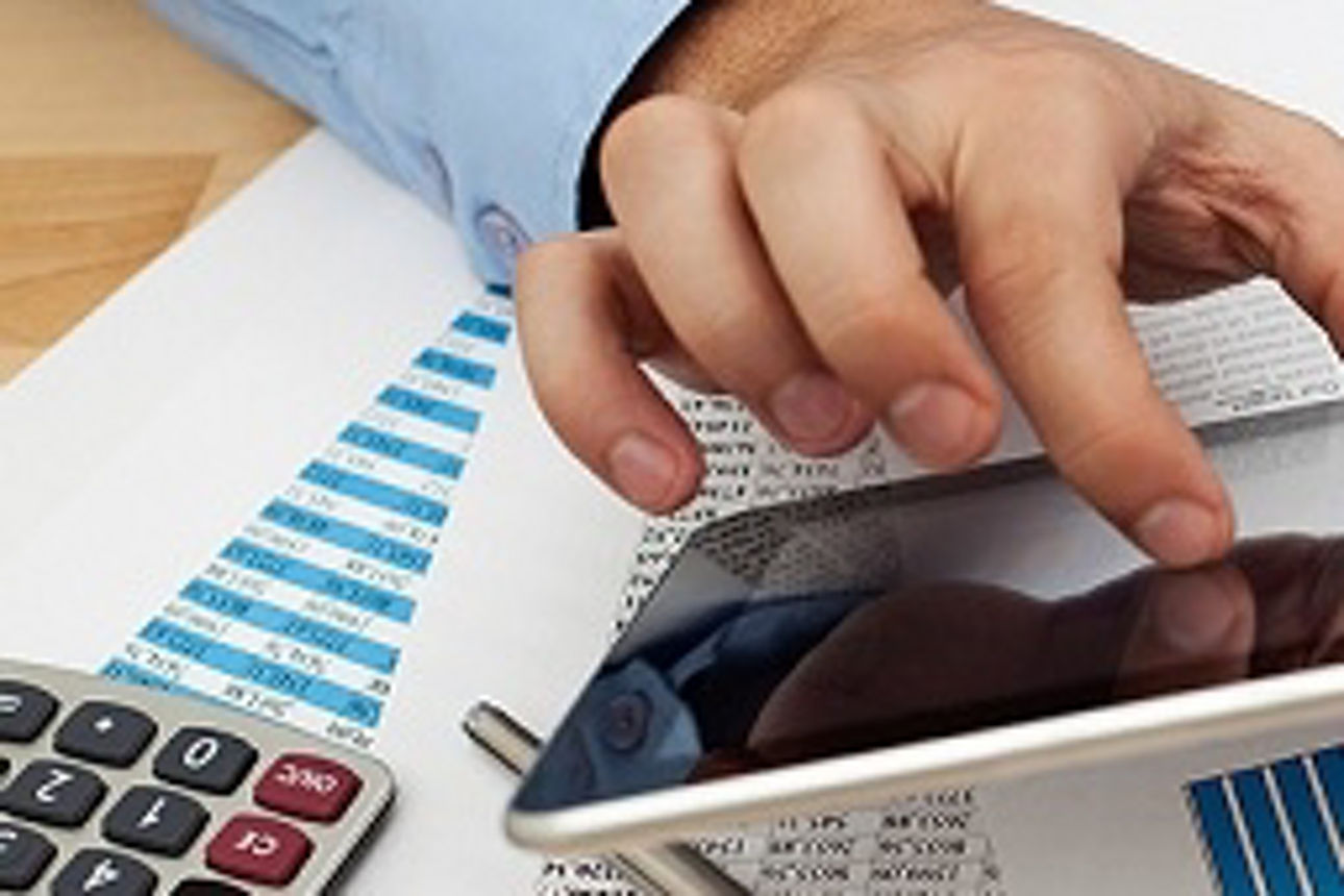 Ein Mann beschäftigt sich mit einem Tablet auf einem Schreibtisch, mit einem Taschenrechner