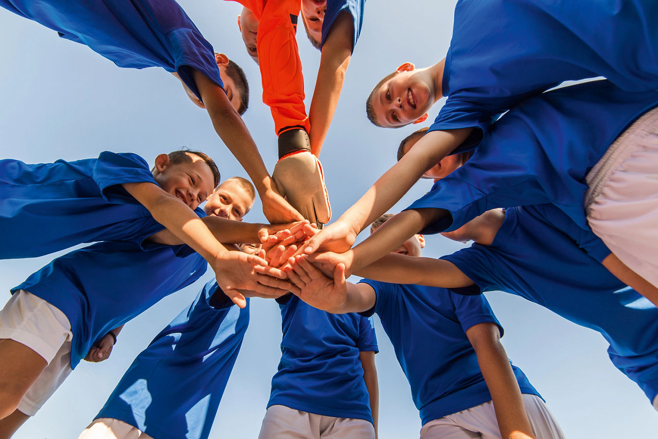 Viele Kinder stehen im Kreis zusammen und halten ihre Hand übereinander