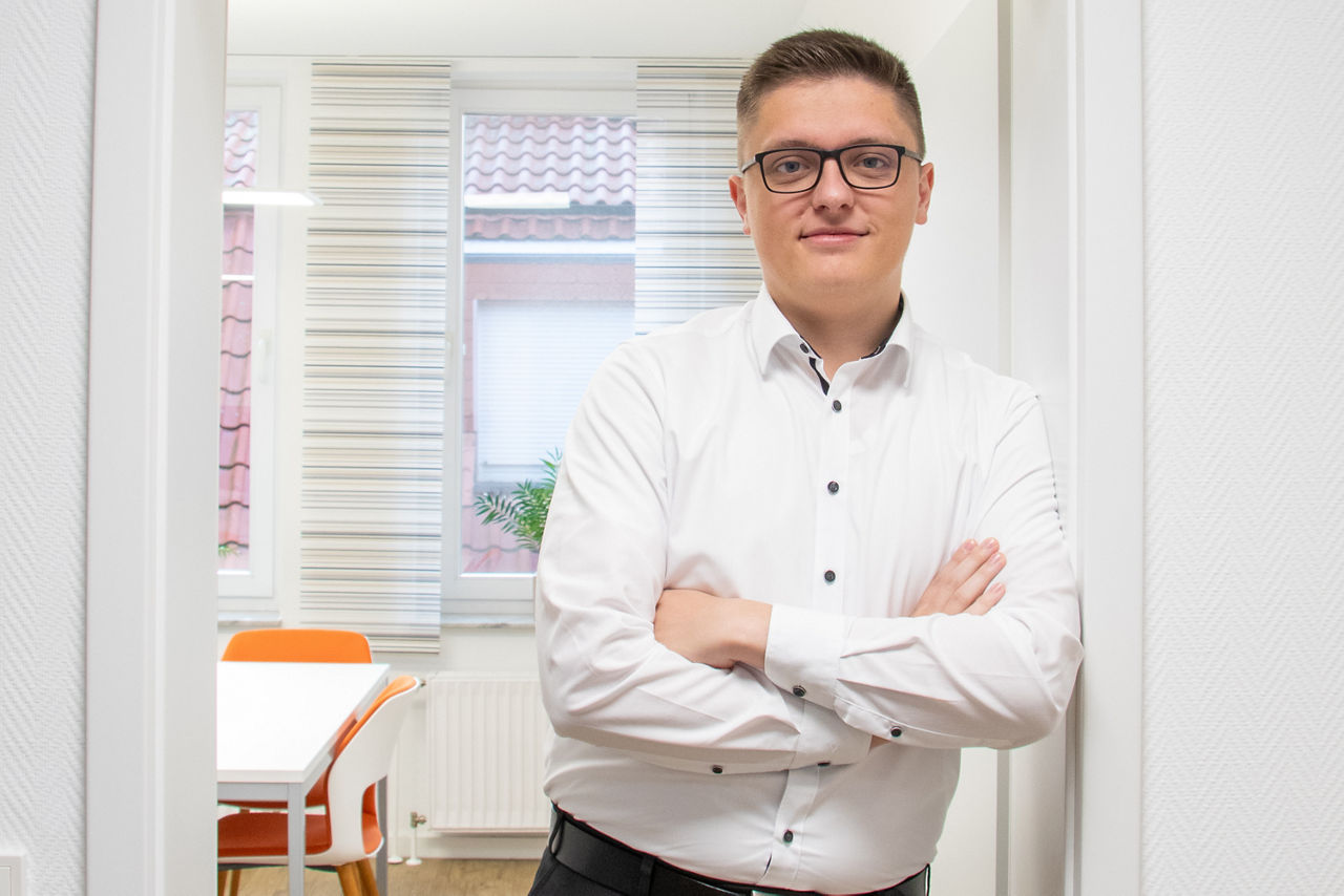 Ein Mann in Hemd steht angelehnt an einen Türrahmen