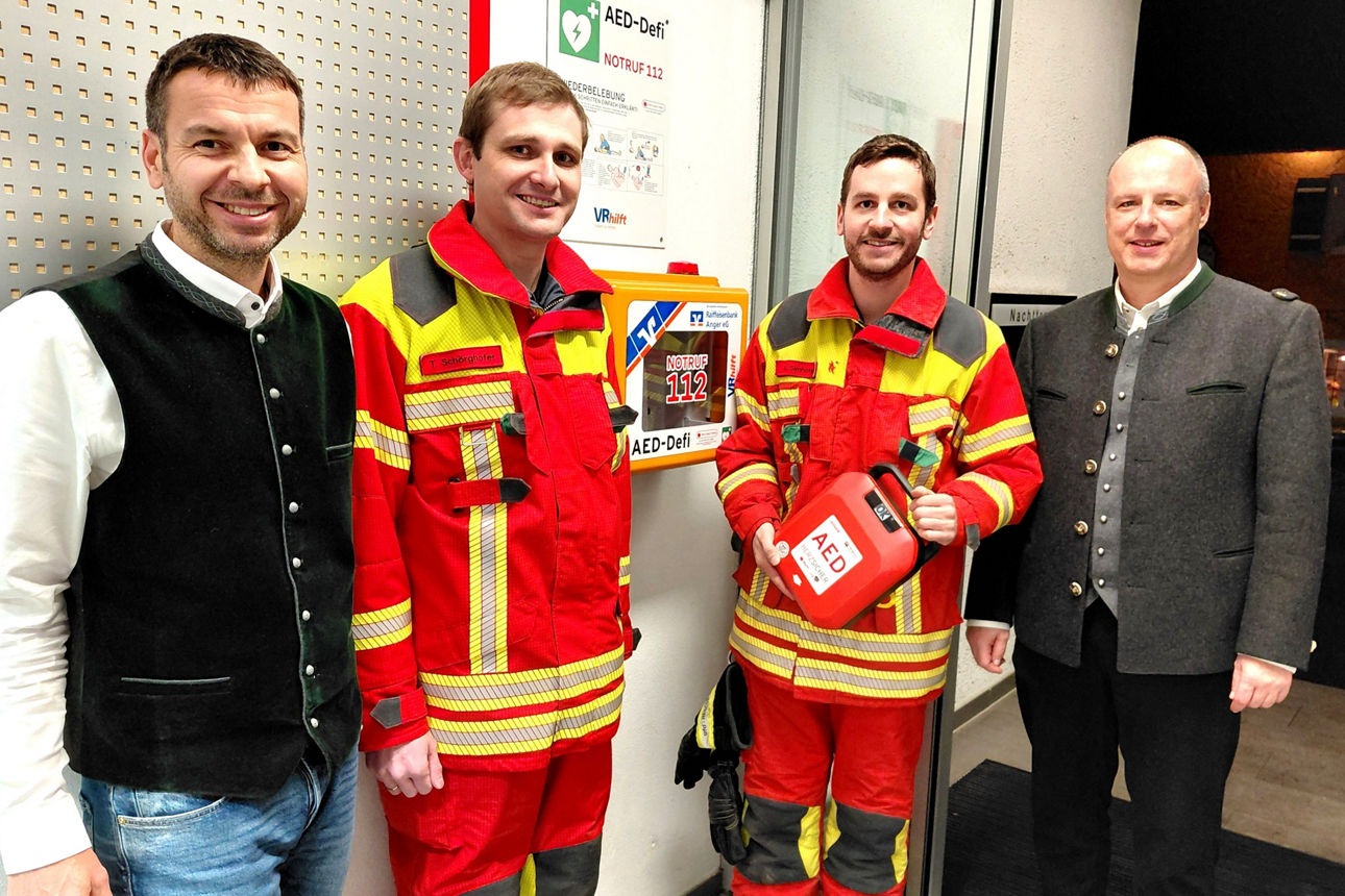 Zwei Feuerwehrmänner in roten und gelben Anzügen und zwei Bankmitarbeiter posieren für das Foto.  