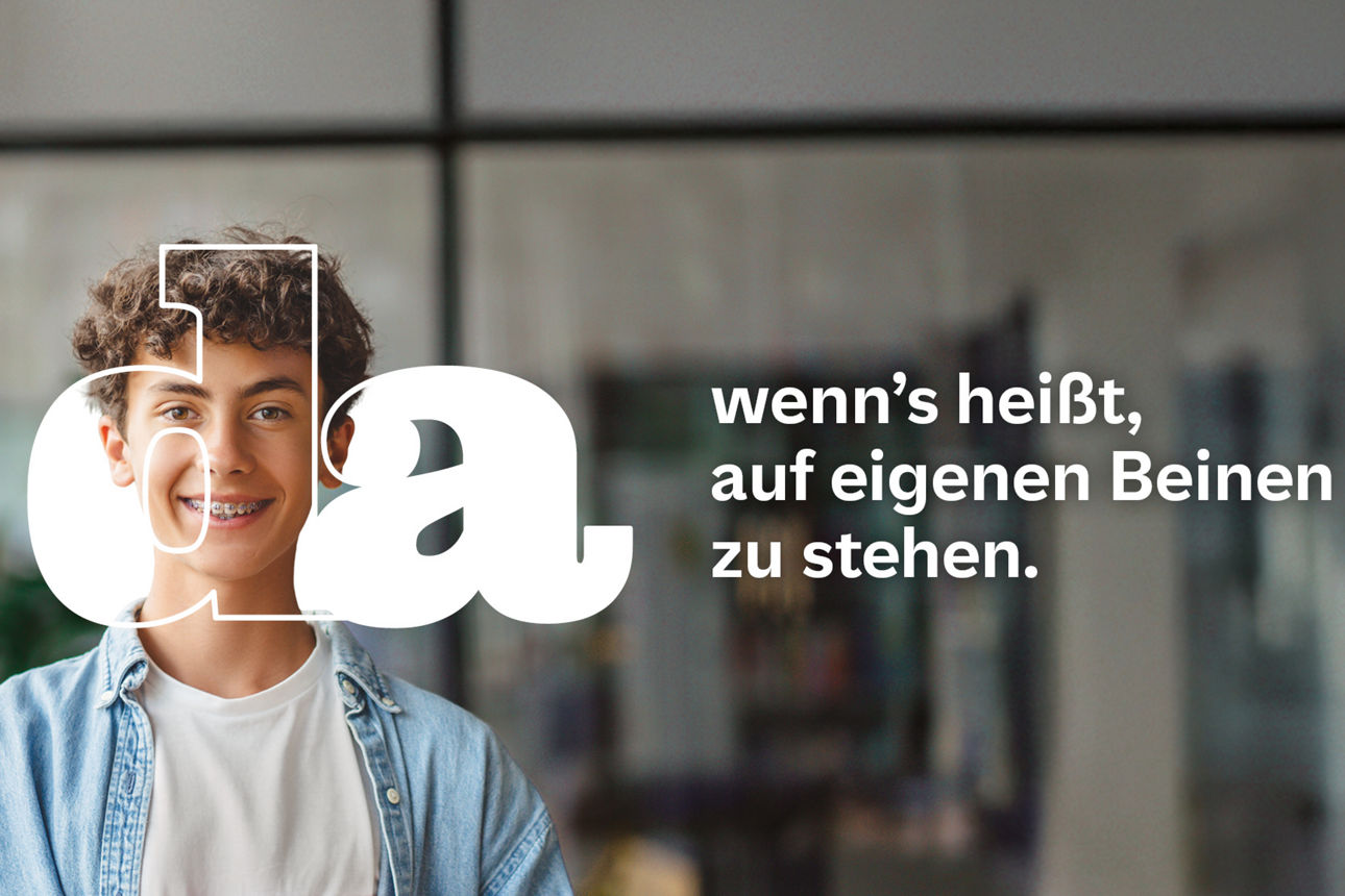 Jugendlicher mit lockigem Haar und Zahnspange steht lächelnd in einer modernen Bibliothek und hält ein rotes Buch