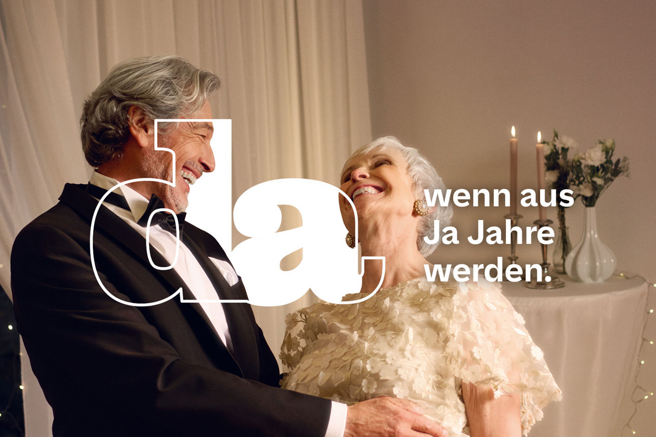 Ein älteres Paar in festlicher Kleidung steht vor einem mit Lichterketten dekorierten Hintergrund