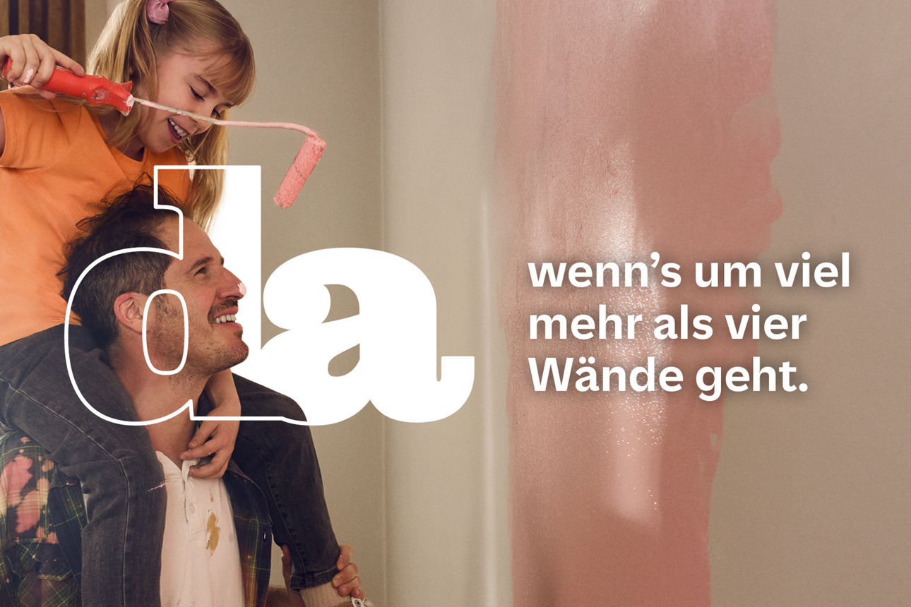 Kind sitzt auf den Schultern eines Erwachsenen und streicht mit einer Farbrolle eine Wand an