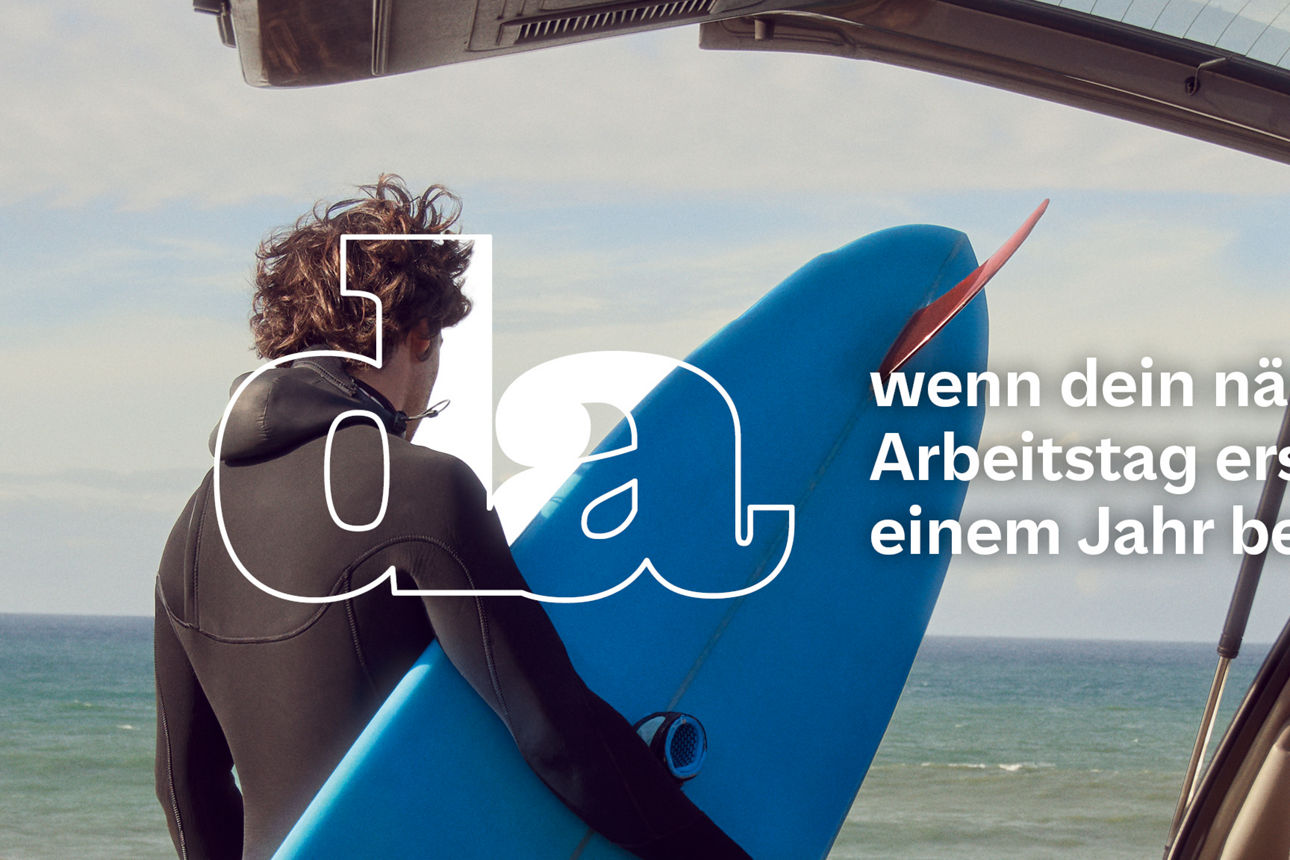 Person im Neoprenanzug hält ein Surfbrett und blickt aufs Meer