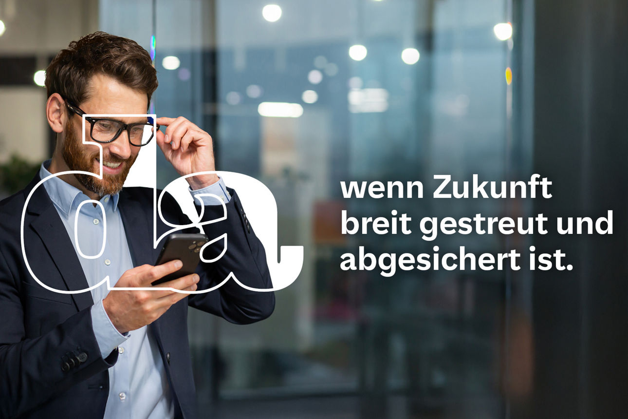 Mann im Business-Outfit steht in modernem Büro und schaut lächelnd auf sein Smartphone während er seine Brille hält