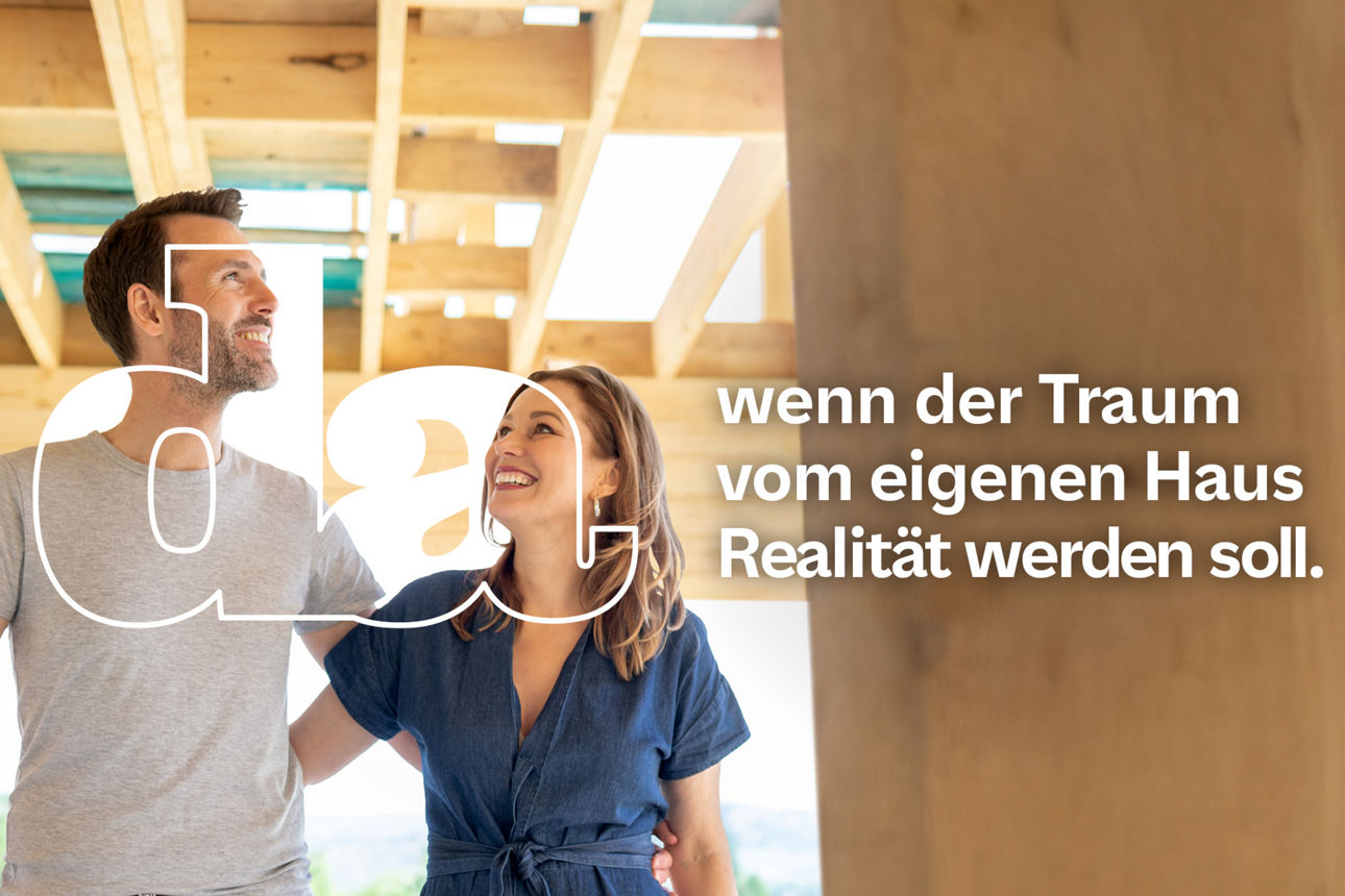 Paar steht in einem Rohbau eines Hauses mit sichtbaren Holzbalken und Balkendecke