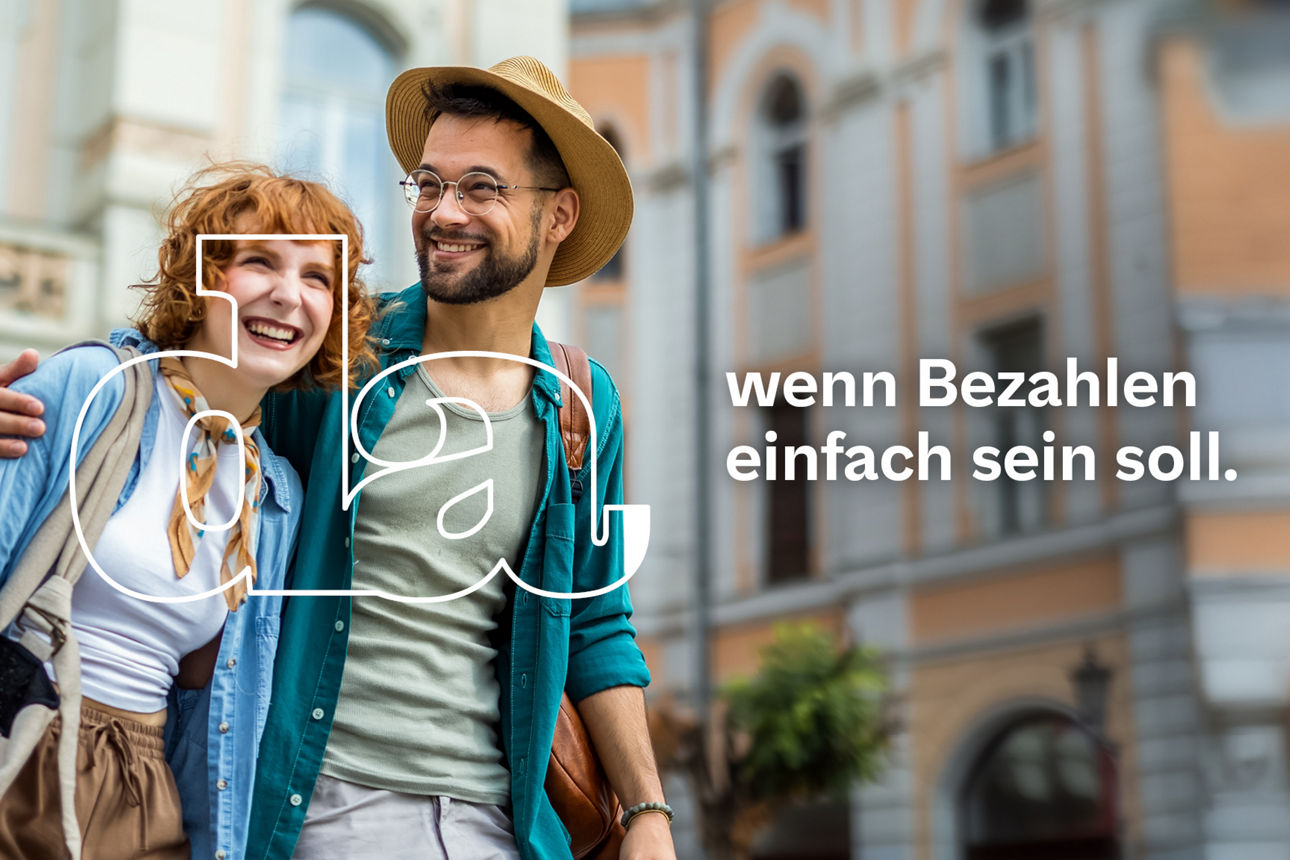 Lächelndes Paar mit Rucksack und Reisetasche schlendert Arm in Arm durch eine historische Altstadt bei sonnigem Wetter