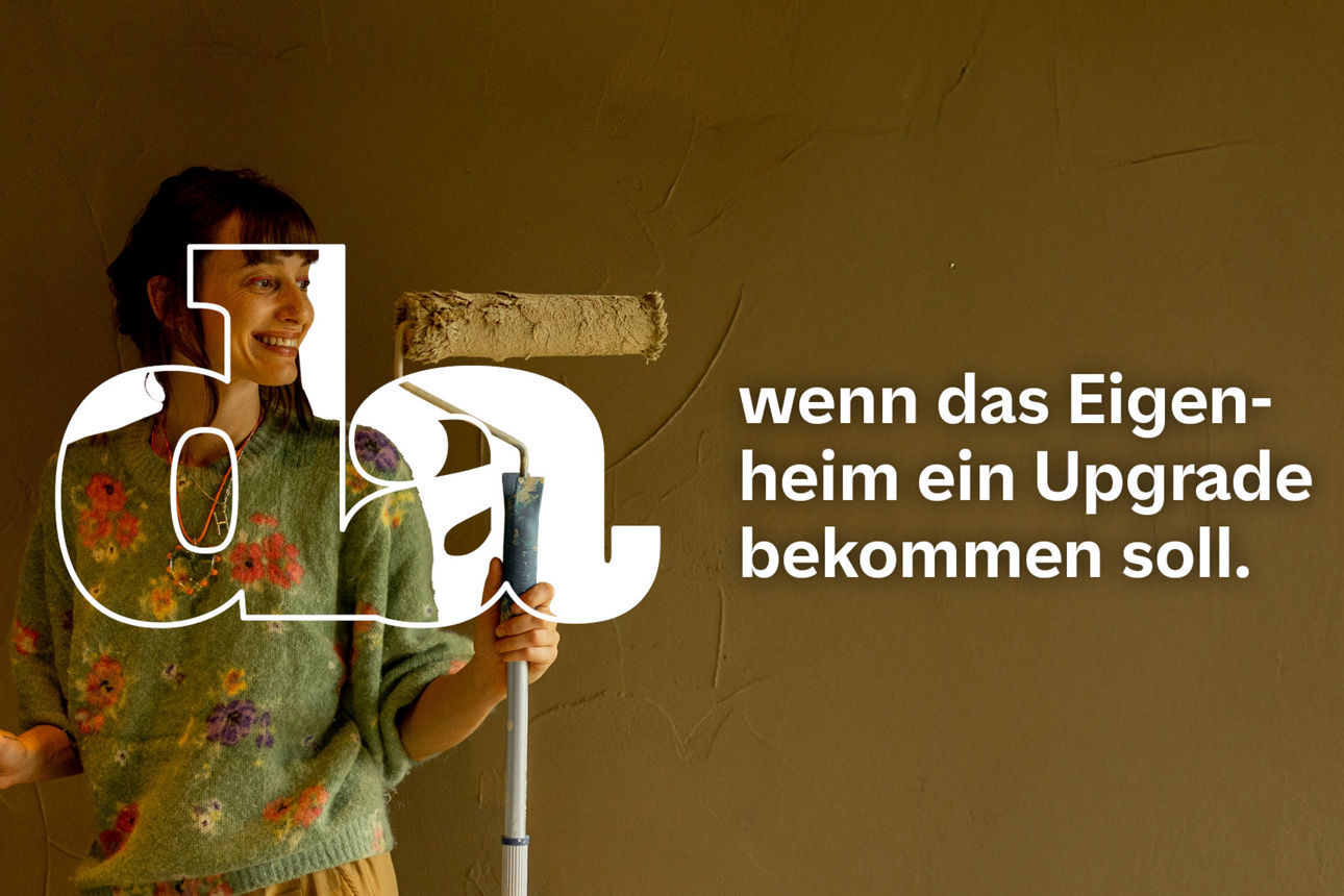 Frau mit Farbrolle steht lächelnd in renovierungsbedürftigem Raum neben einer Leiter und schaut Richtung Fenster