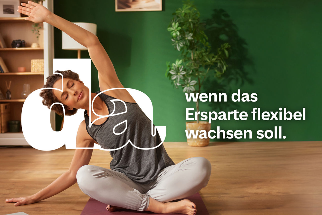 Frau sitzt im Schneidersitz auf einer Yogamatte im Wohnzimmer macht eine Dehnübung mit erhobenem Arm.