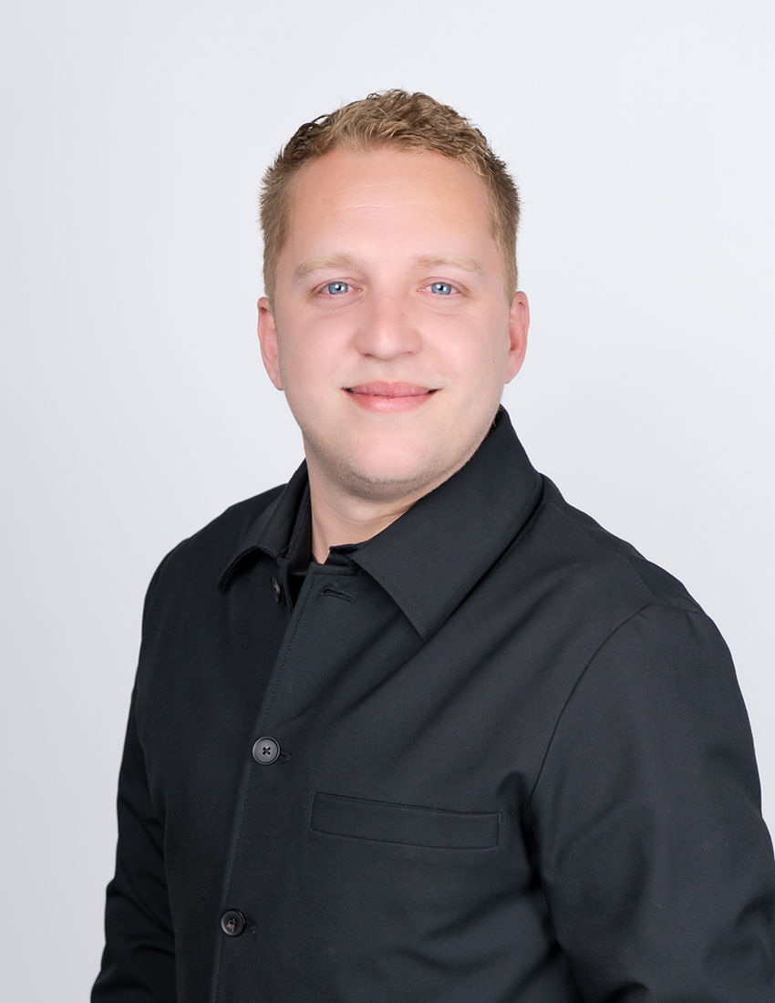 Foto unseres Vermögensberaters Dennis Gulba vor einem grauen Hintergrund mit einem schwarzen Hemd