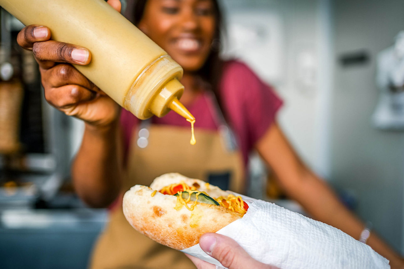 Eine Frau macht Senf auf einen Hotdog.