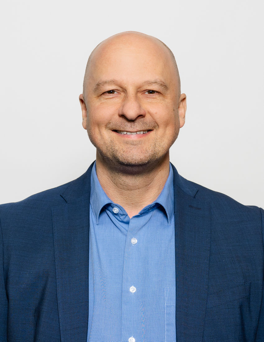 Foto unseres Vermögensberaters Roman Weigler vor einem grauen Hintergrund in einem blauen Jackett