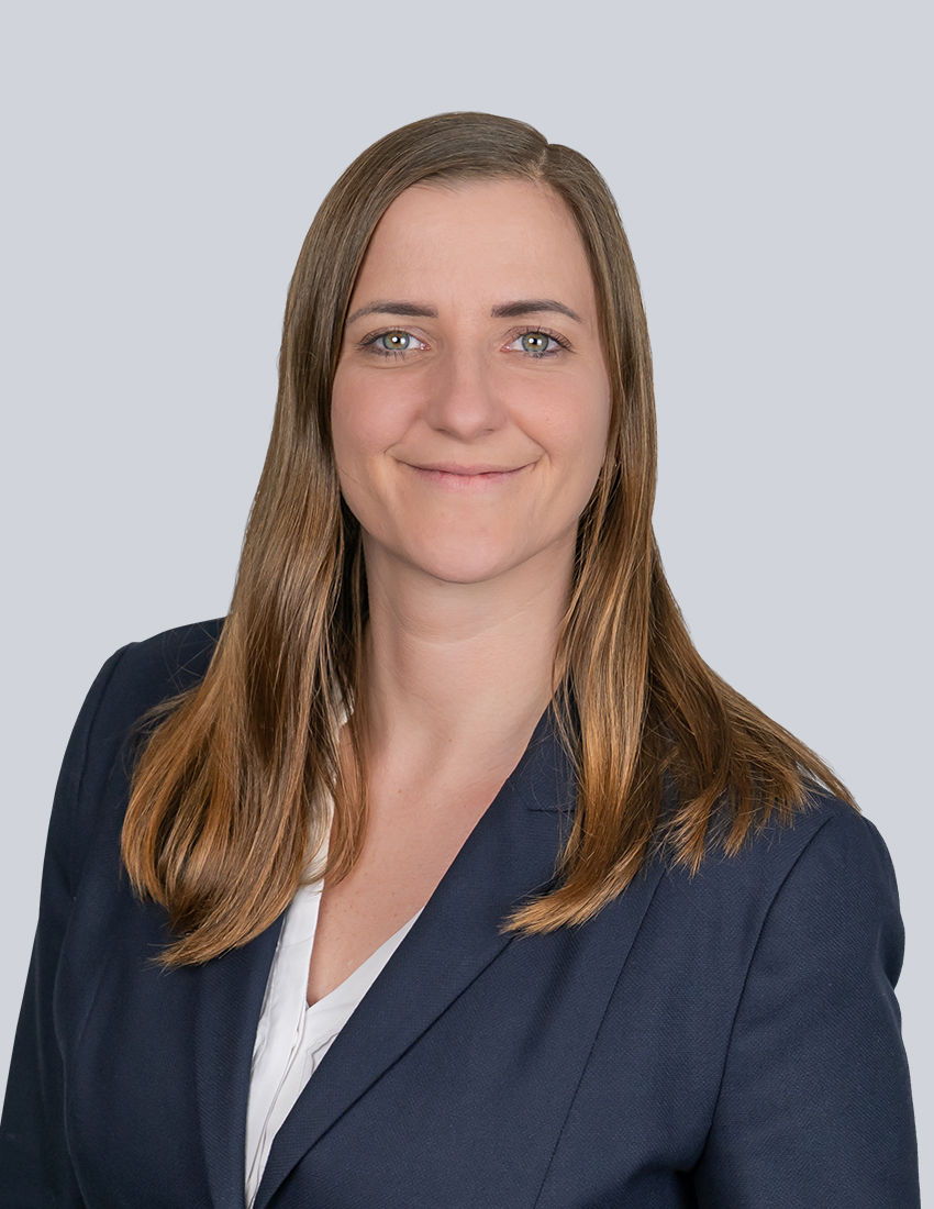 Foto unserer Kundenberaterin Linda Schurz vor einem grauen Hintergrund in einem blauen Blazer