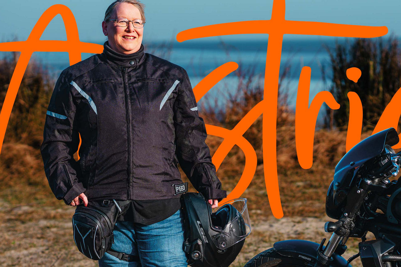 Frau mit Motorrad am Strand.