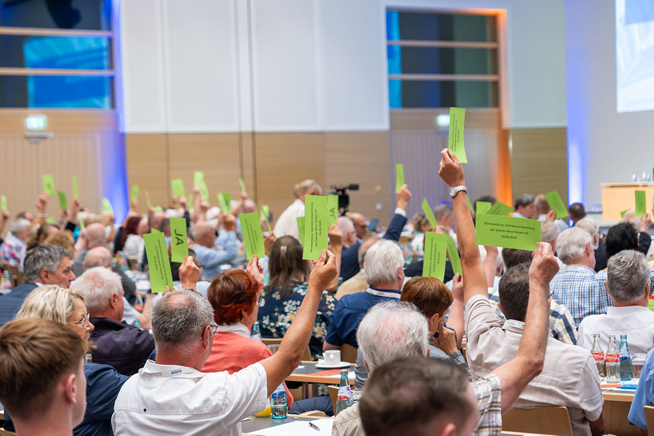 Eine Totale von der Vertreterversammlung mit mit einem Teil der Vertreter, während sie grüne Stimmkarten hochhalten.