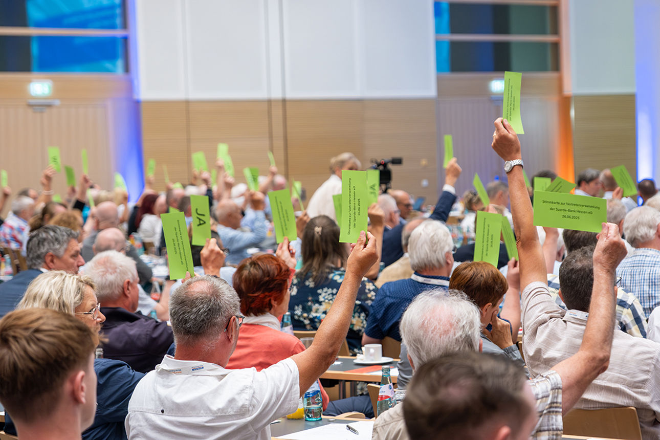 Eine Totale von der Vertreterversammlung mit mit einem Teil der Vertreter, während sie grüne Stimmkarten hochhalten.