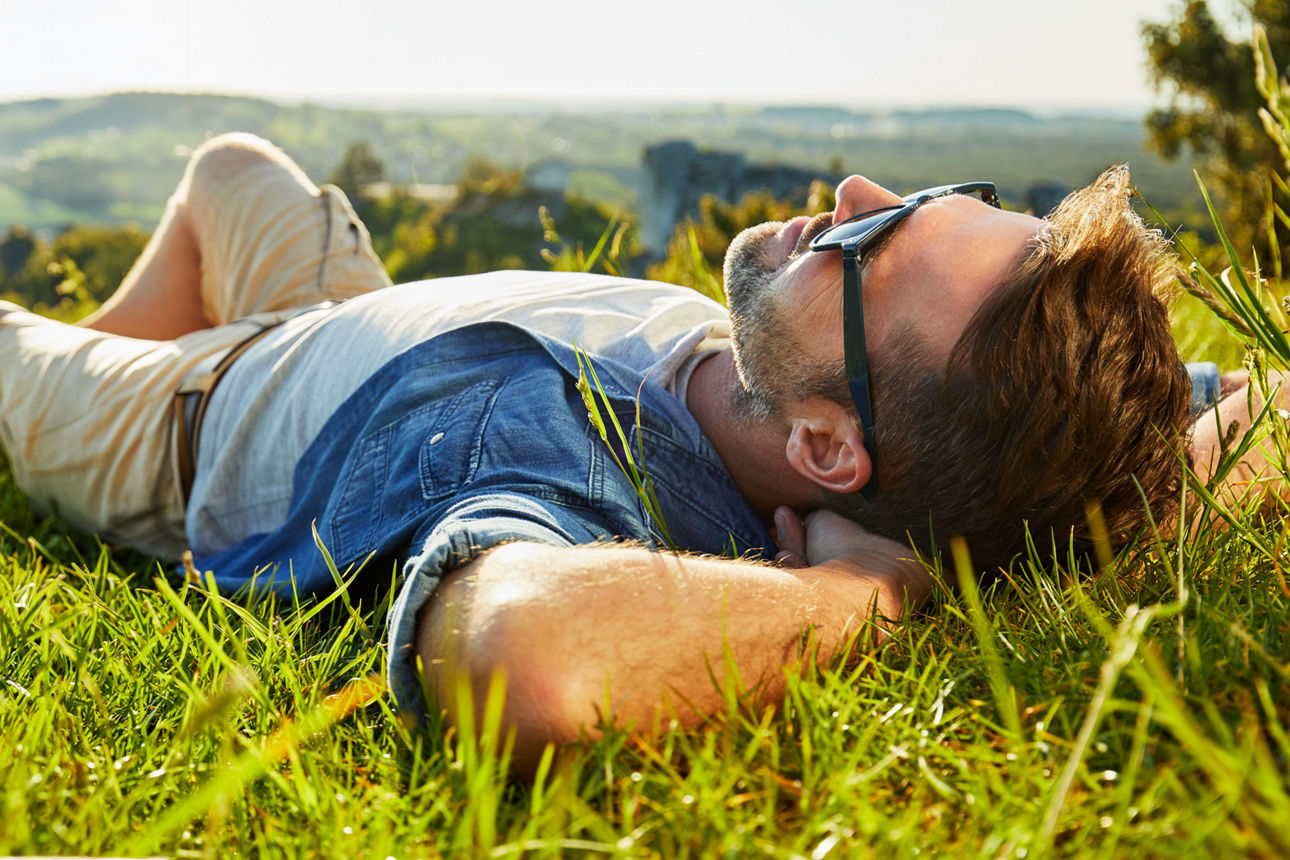 Mann entspannt auf Wiese in der Natur, liegt im Gras bei sonnigem Wetter