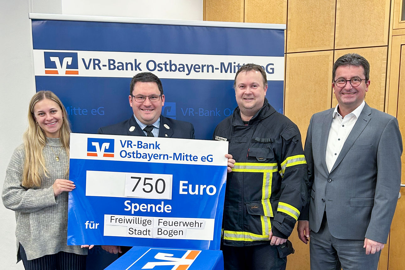 Drei Männer und eine Frau lächeln in die Kamera und halten einen Spendenschein hoch