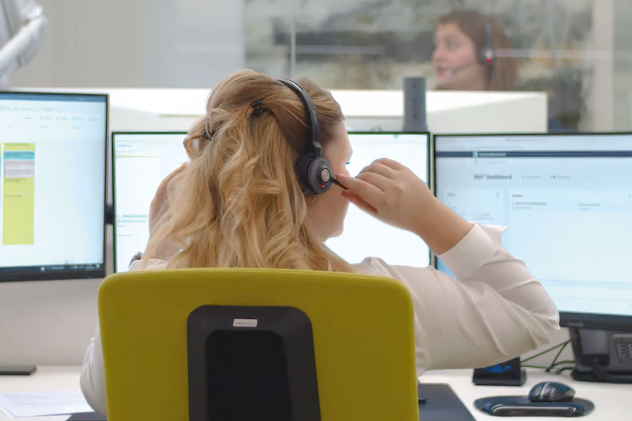 Frau mit Headset auf dem Kopf sitzt vor mehreren Bildschirmen