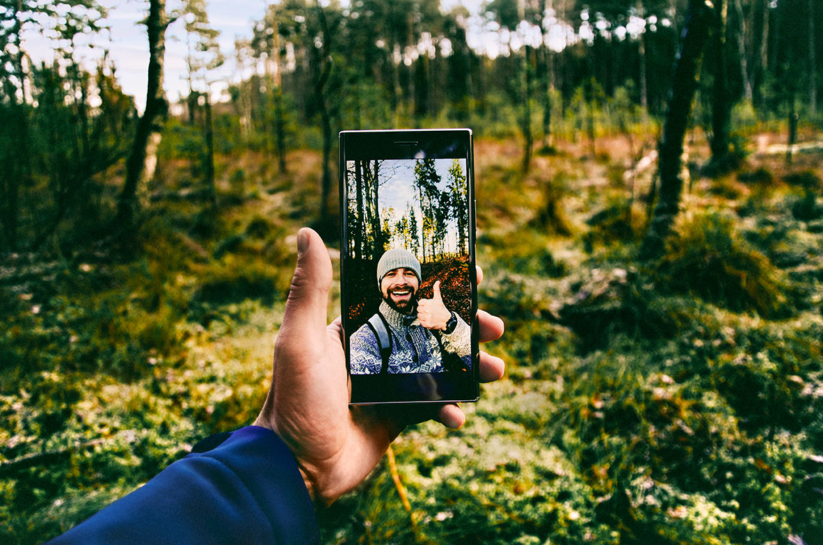 Mann steht im Wald und macht ein Foto von sich selber