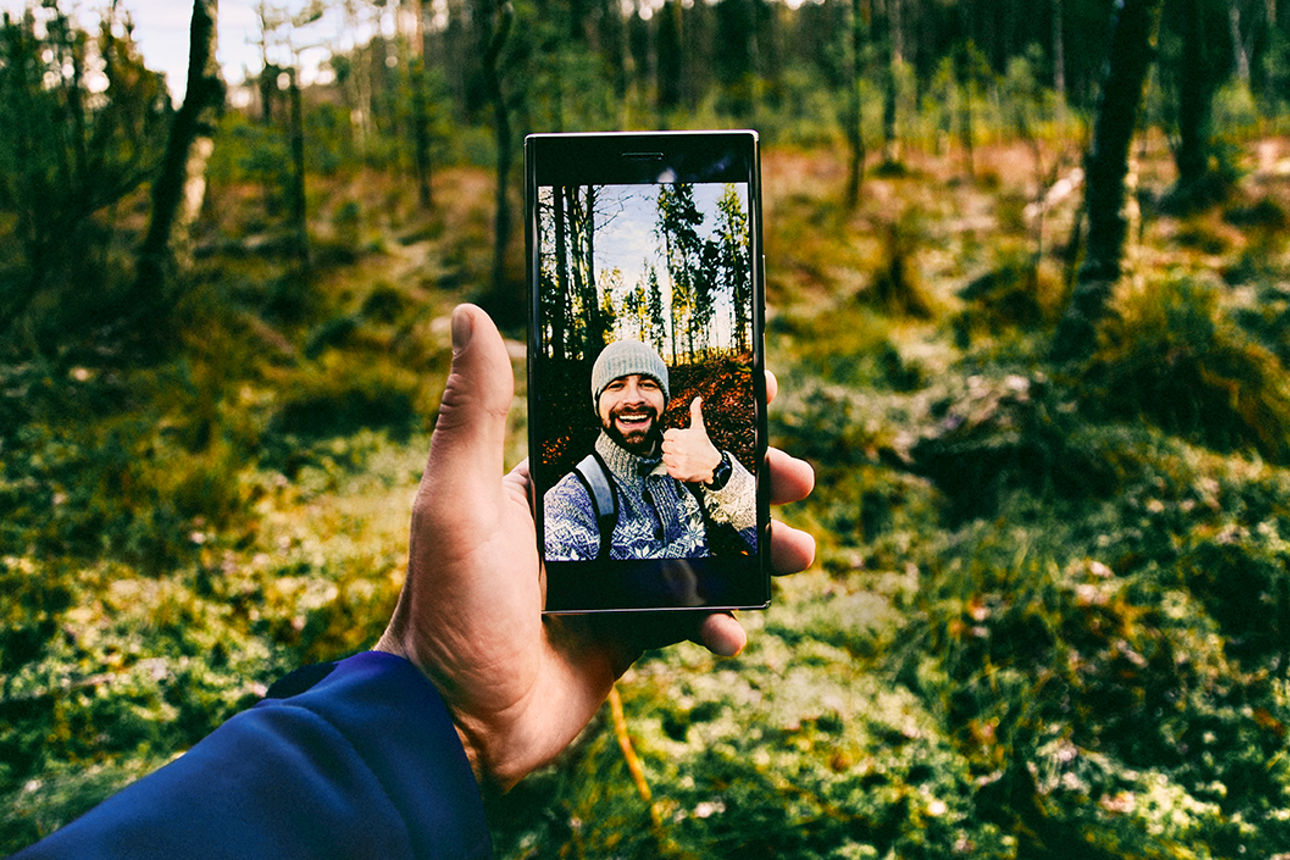 Mann steht im Wald und macht ein Foto von sich selber