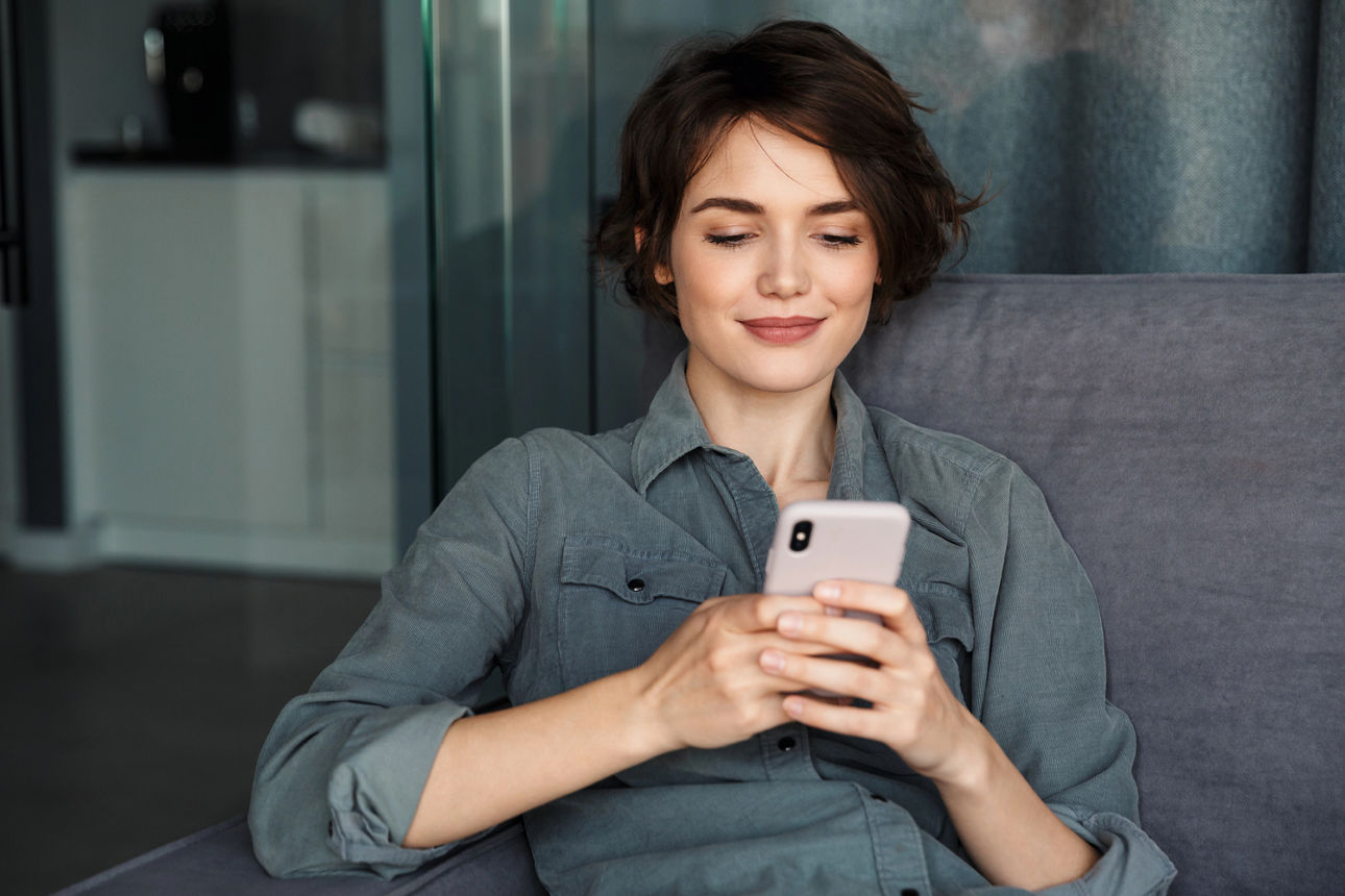 Frau mit Handy in der Hand sitzt auf einem Sessel