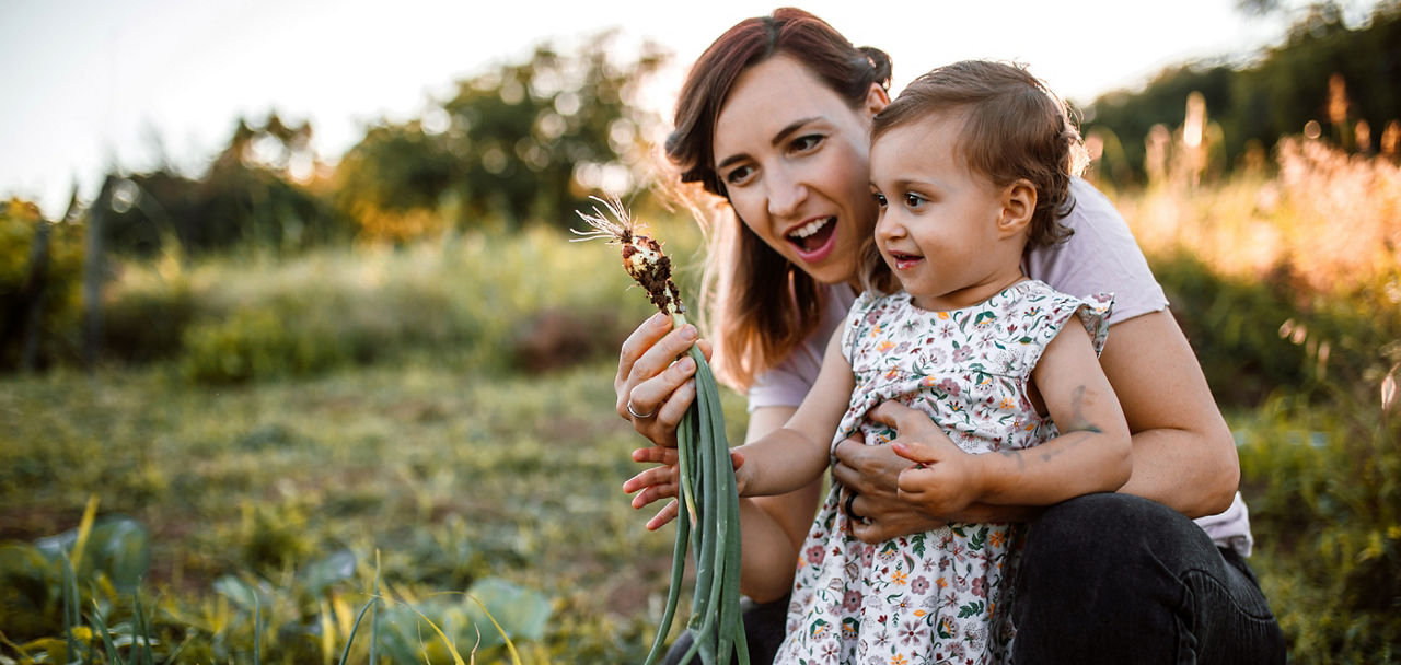 Mutter und Kind schauen sich auf einer Wiese eine Blumenwurzel an.