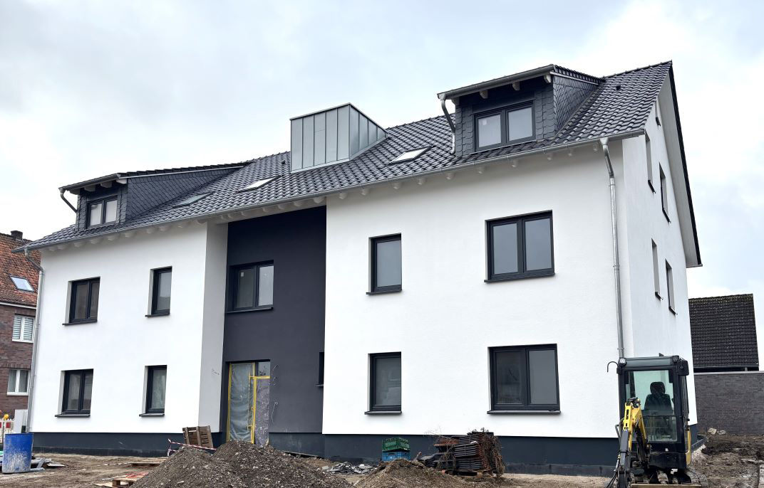 Ein modernes Haus mit einer weißen Fassade und einem schwarzen Dach.