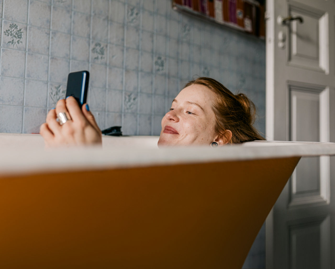 Frau liegt mit Smartphone in der Badewanne
