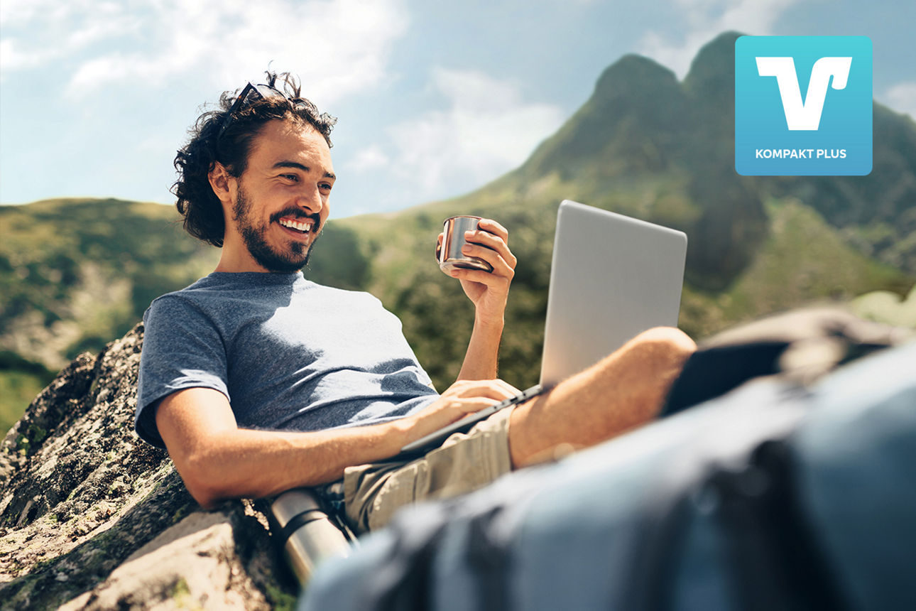 Mann in den Bergen mit Laptop auf dem Schoß und Kaffee in der Hand