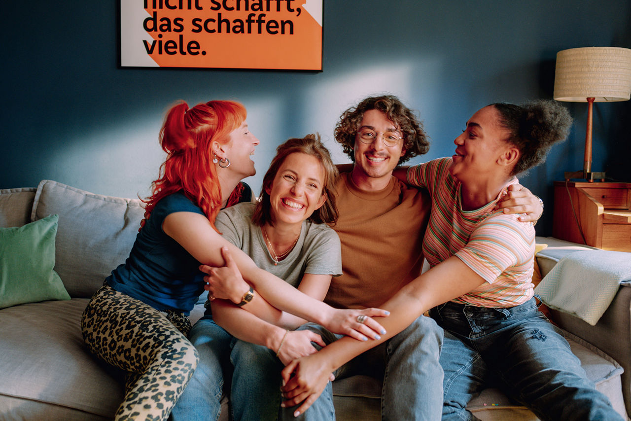 Vier junge Leute sitzen lachend auf einem Sofa 