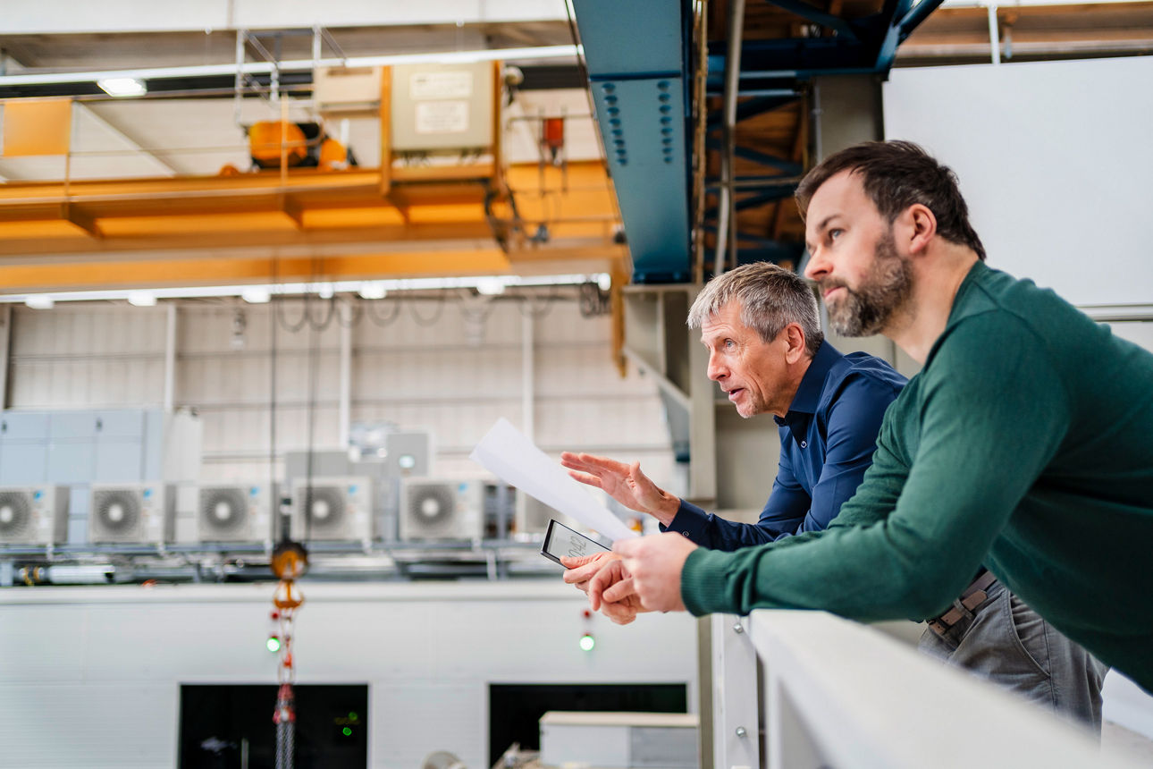 Businessman and manager discussing over document leaning on railing in industry