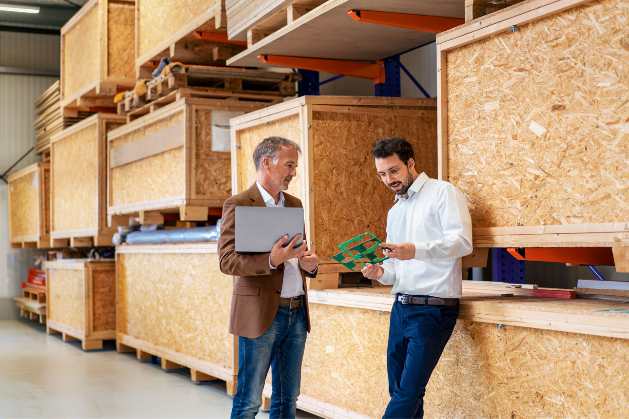 Busisnessman hält einen Laptop und disskutiert über ein Mutterboard im Warenlager.
