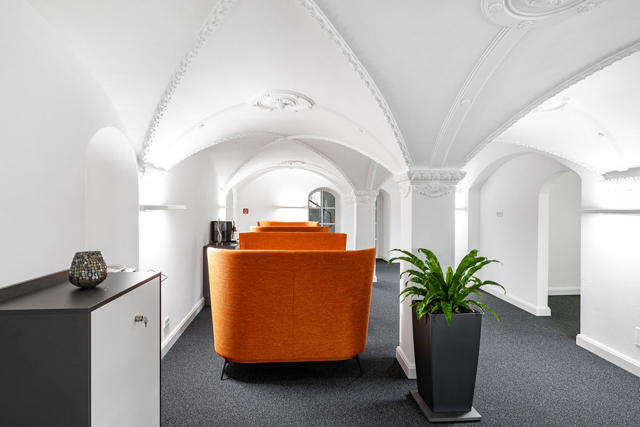 Wartebereich mit dunklem Teppich und orangen Sitzgelegenheiten