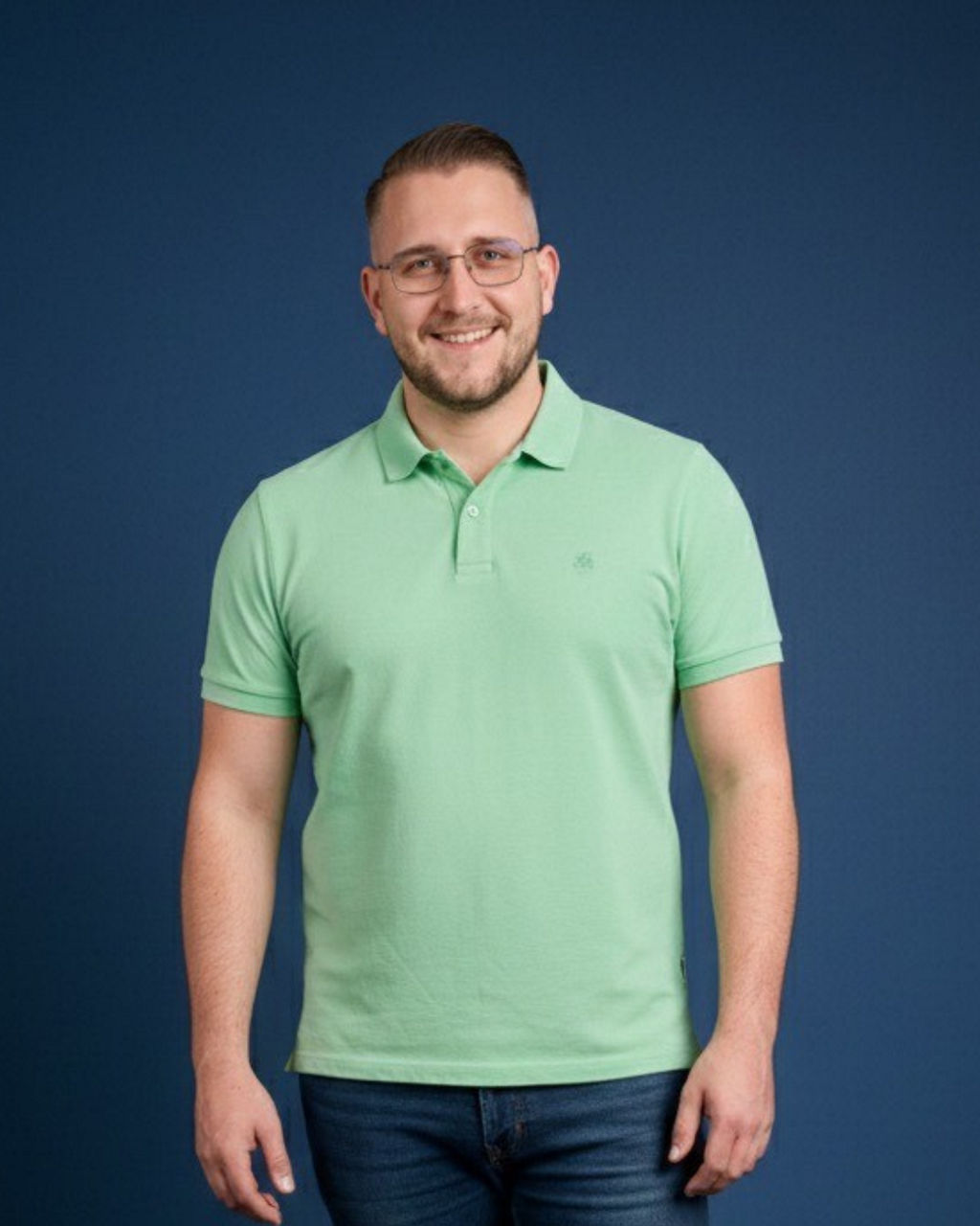 Lächelnder Mann mit Brille in grünem Poloshirt vor blauem Hintergrund